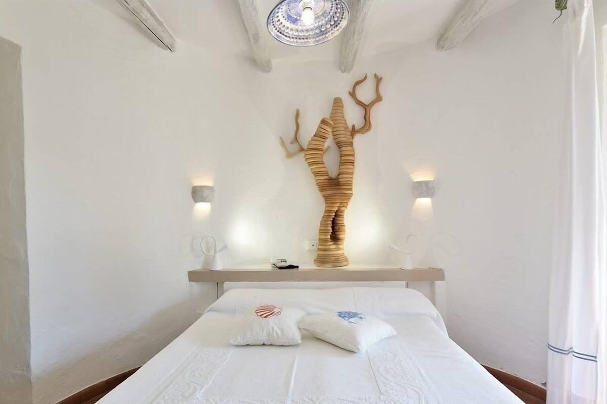 Un dormitorio con una cama, una escultura de madera en la pared y dos apliques.