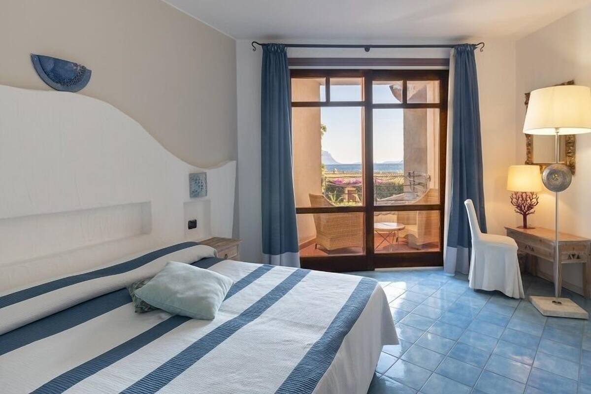 Habitación de hotel con cama, una silla, una mesa, una lámpara y vistas al exterior.