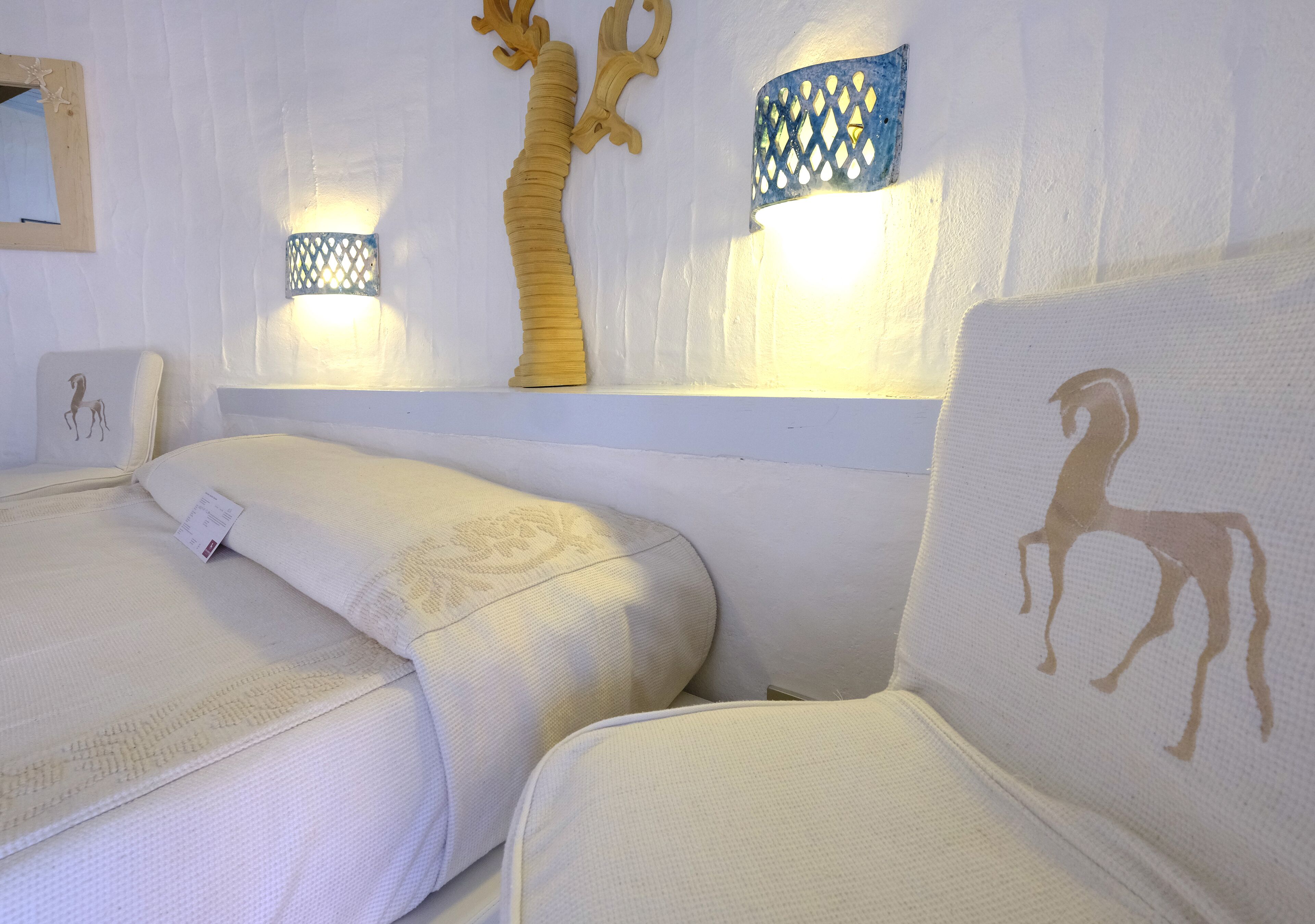 A hotel room with two beds, a decorative wall with a tree and wall sconces, and a framed picture on the wall.