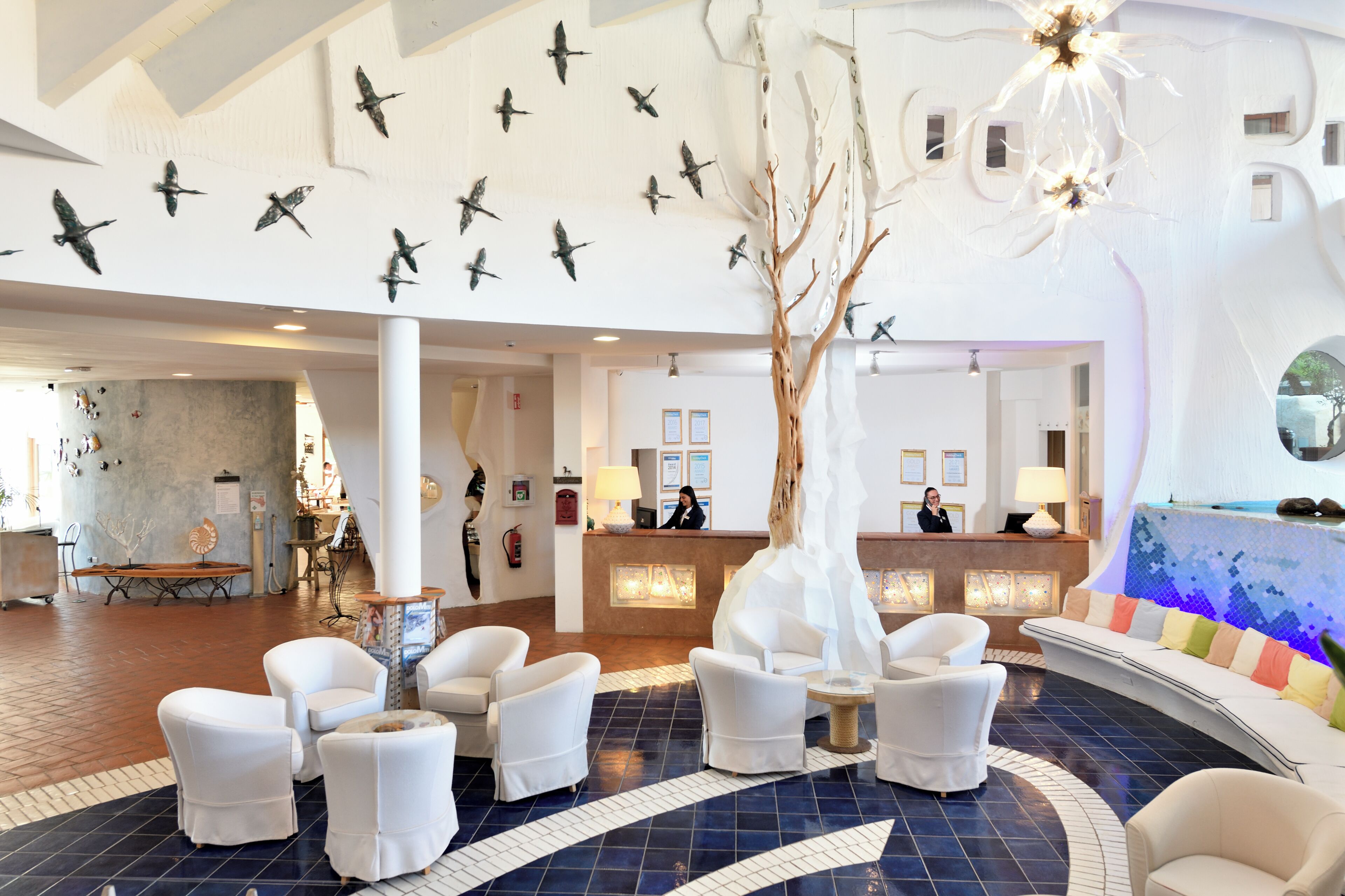 A lobby with a reception desk, white chairs, a decorative tree, and wall-mounted bird art.