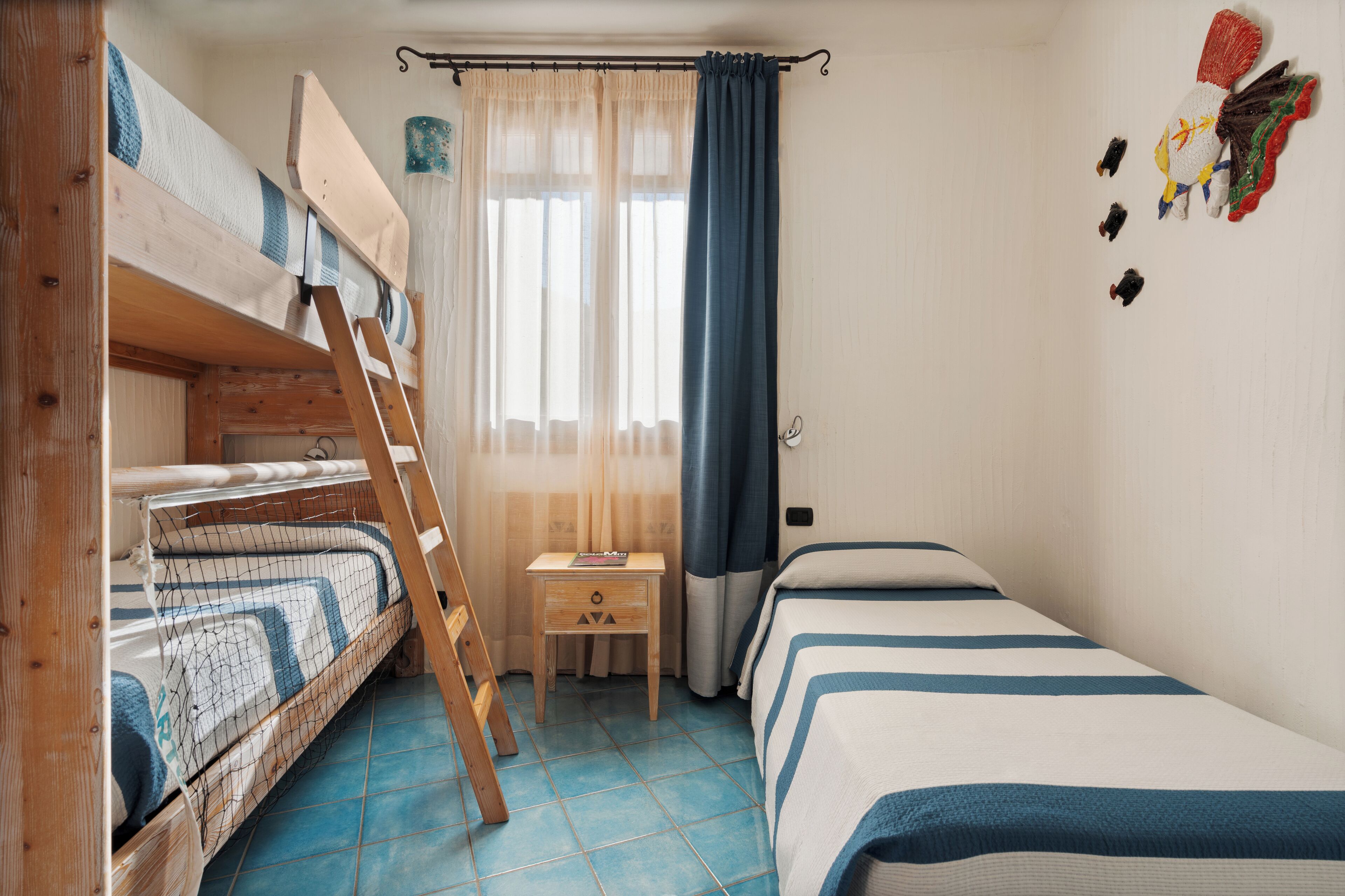 A room with bunk beds, a small bedside table, and a window with curtains.