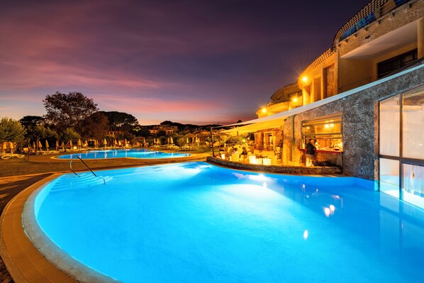 Une piscine avec vue sur le coucher de soleil, un bâtiment à la façade en pierre et un espace bar.