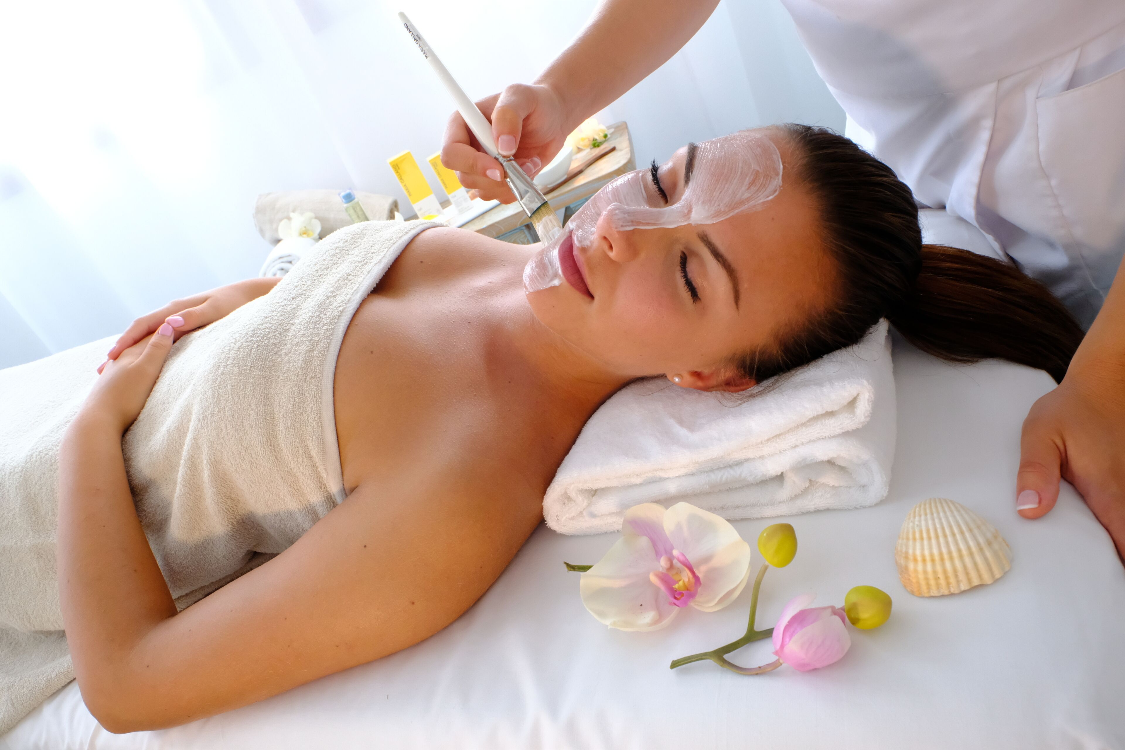 A person lying on a bed with a towel, a face mask, and a seashell.