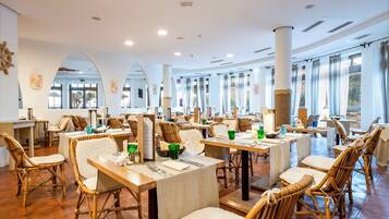Un restaurante con mesas altas y sillas de mimbre, ventanas amplias y suelo de baldosas.