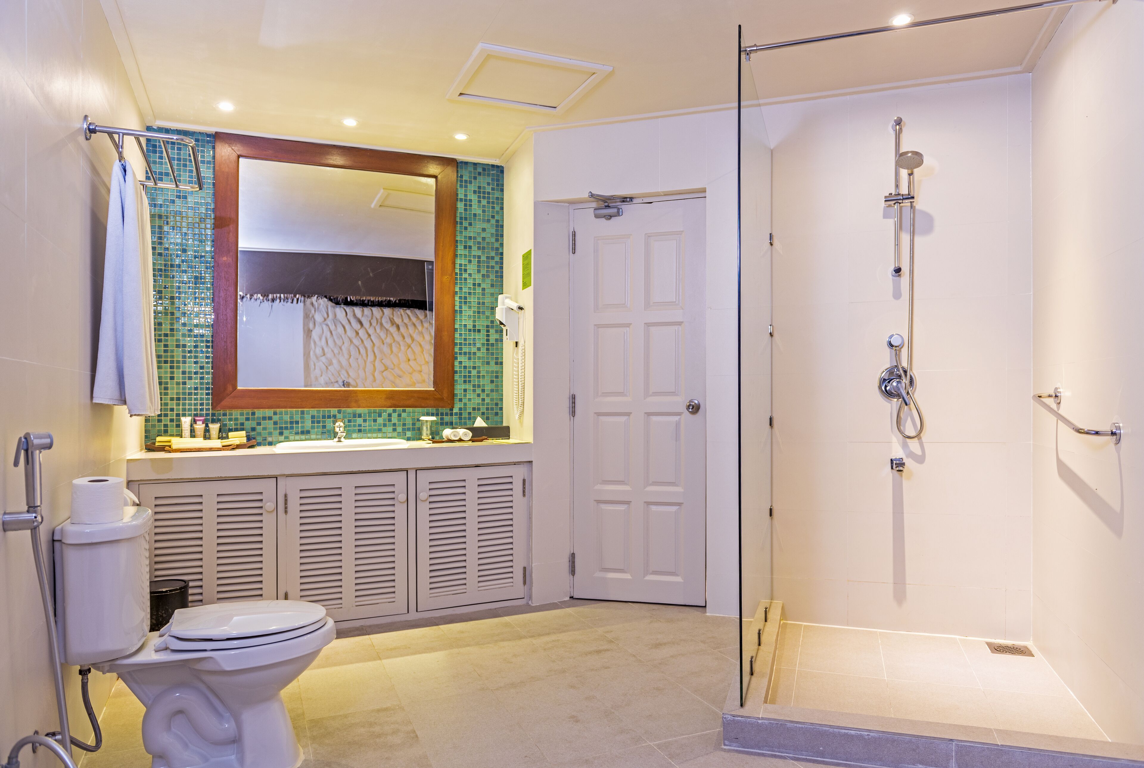 Een badkamer met toilet, wastafel, spiegel, douche en betegelde wanden.