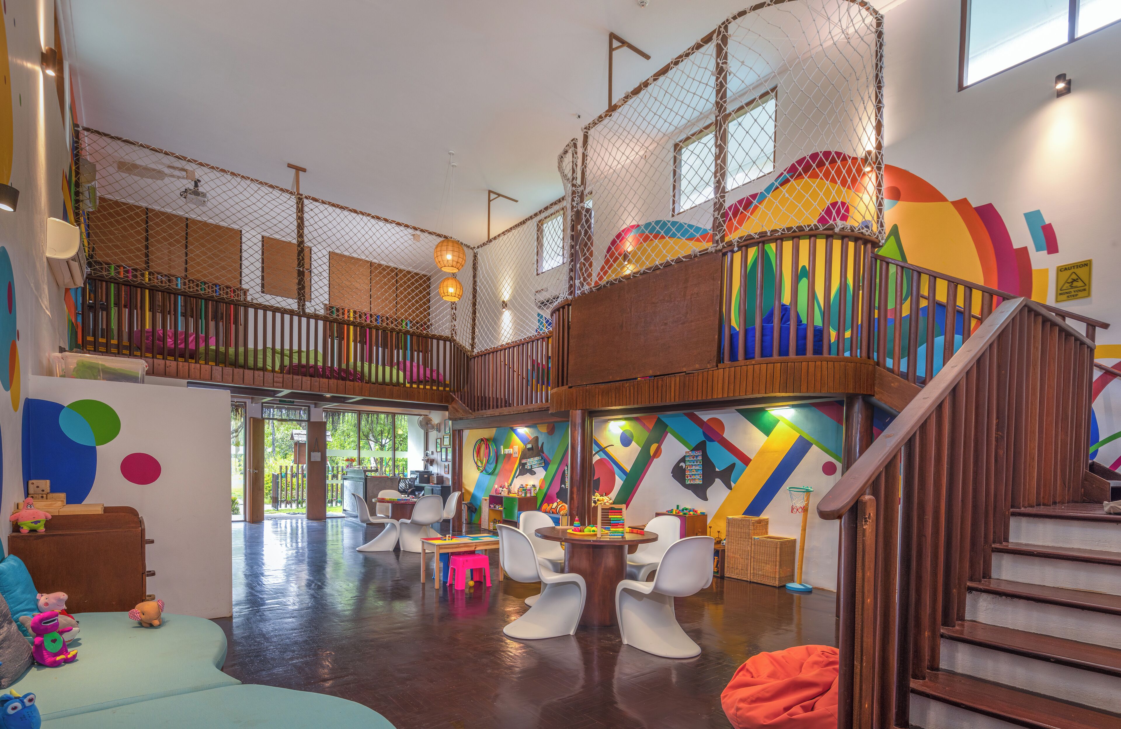 A spacious indoor play area with a wooden staircase, colorful walls, and various play furniture.