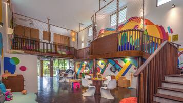 A spacious indoor play area with a wooden staircase, colorful walls, and various play furniture.