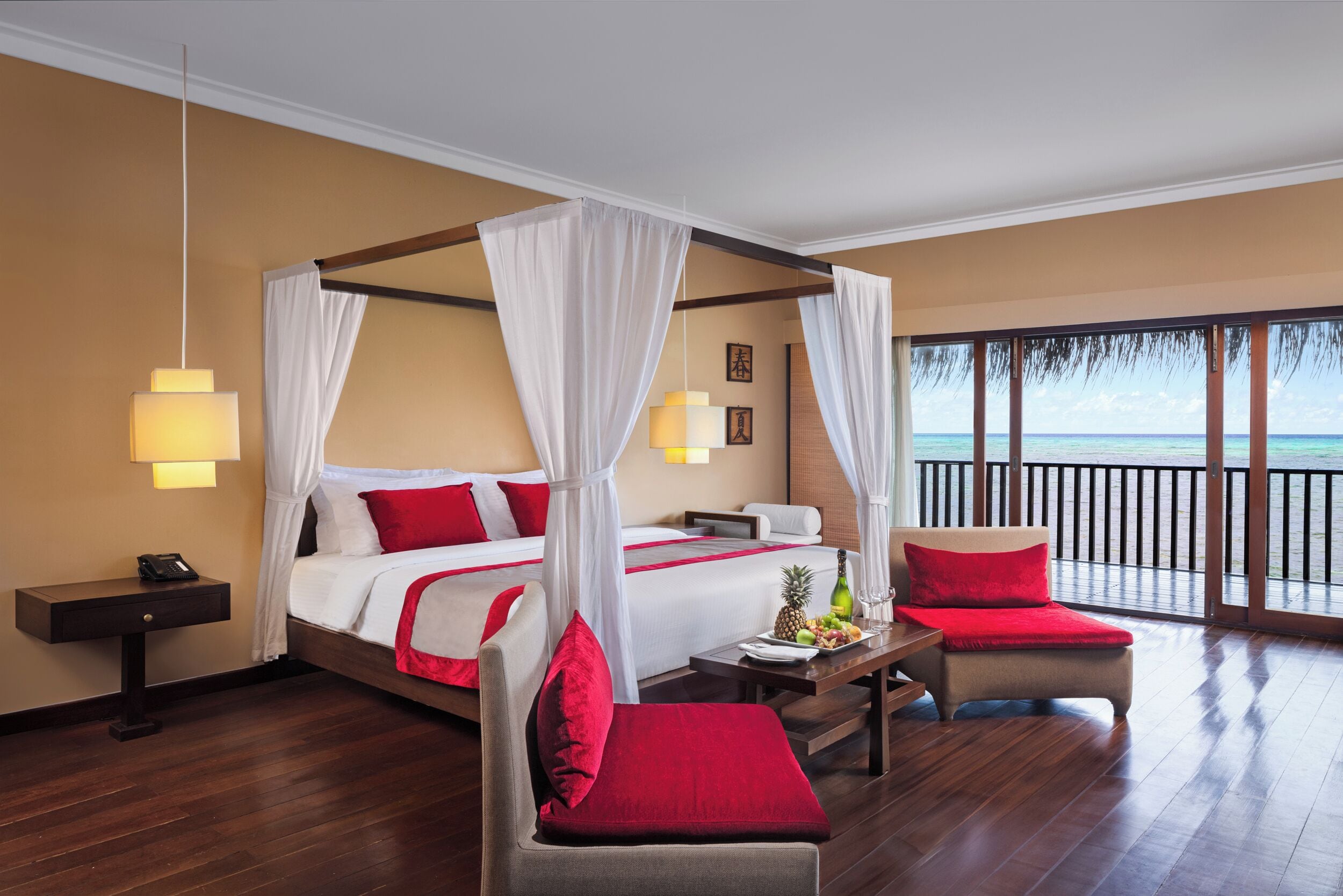 Habitación de hotel con cama con dosel, balcón con barandilla, suelo de madera y mesita de noche con lámpara.