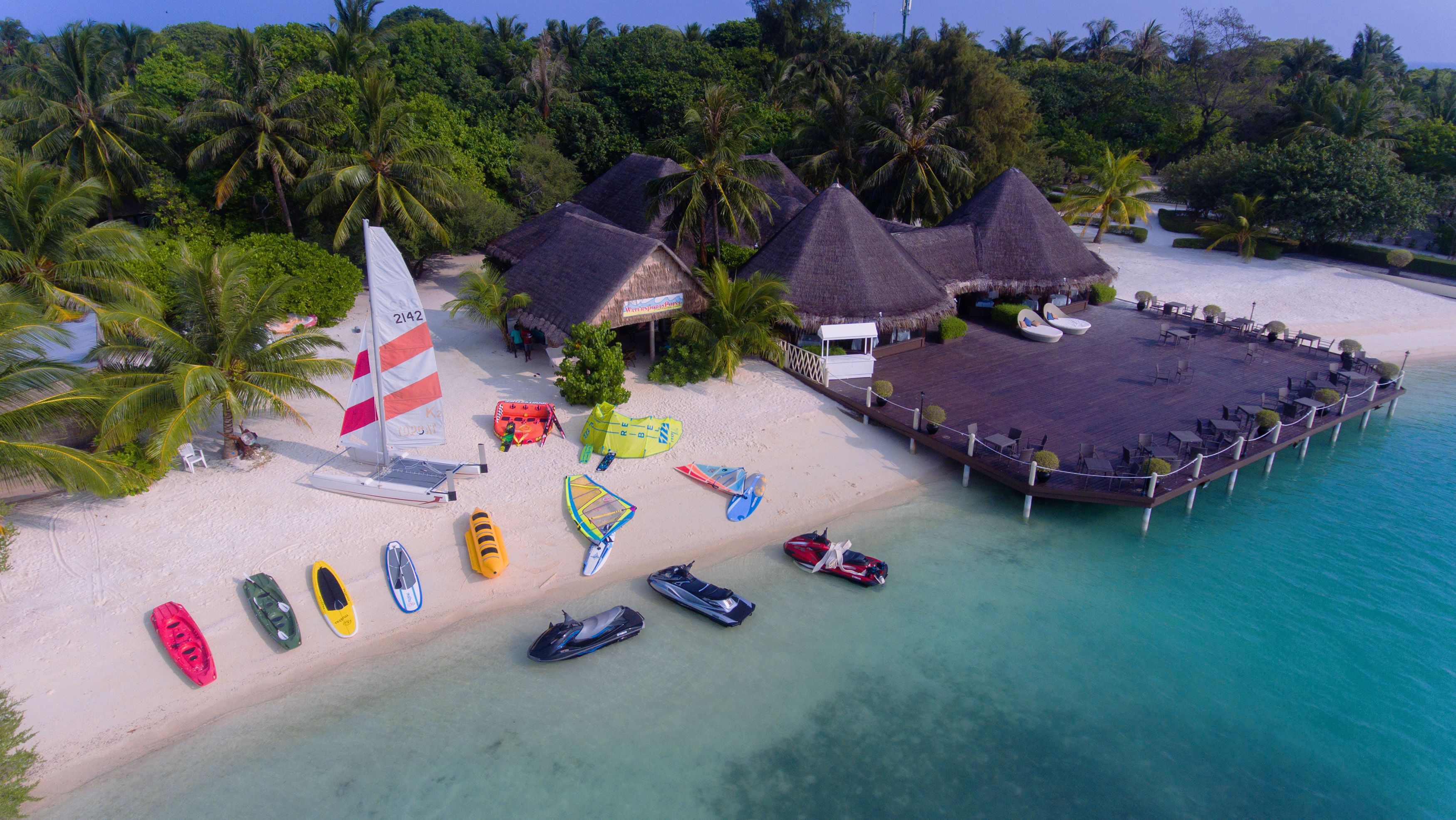 A beachside resort with thatched-roof huts, a sandy beach, and various water sports equipment.