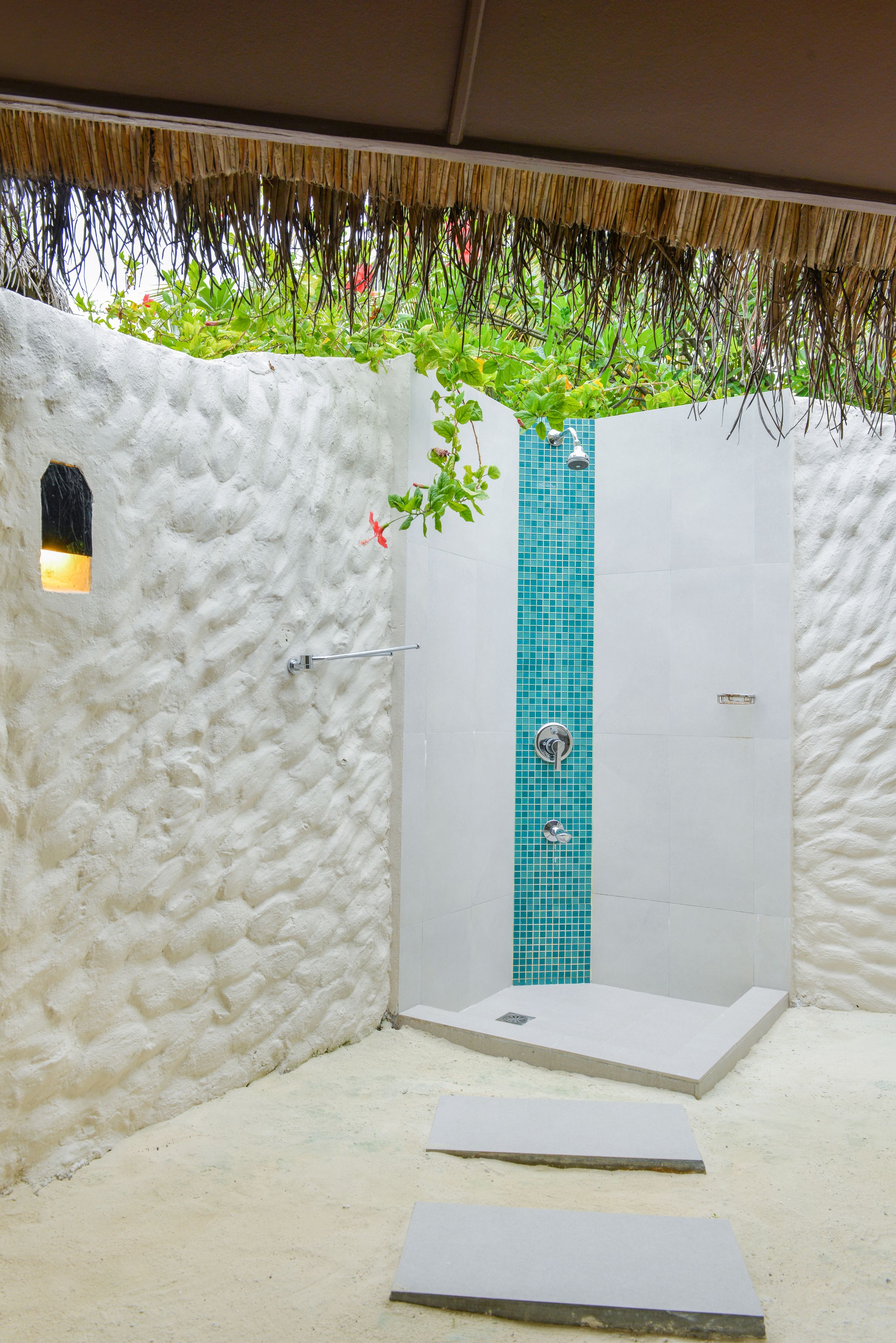 A shower area with a white textured wall, a blue-tiled shower panel, and a small window.