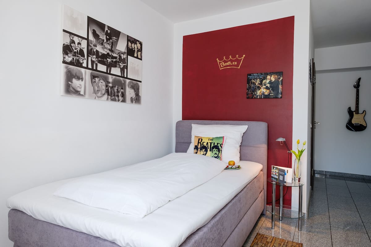 Un dormitorio con una cama, una pared de acento roja y un cartel de The Beatles.