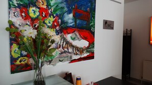 Una habitación con un cuadro abstracto grande en la pared, un florero con flores sobre una mesa y un periódico.