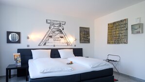 Una habitación de hotel moderna con una cama grande, una mesita, una silla y obras de arte en las paredes.