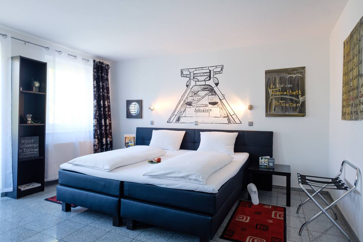 Un dormitorio moderno con una cama grande, una mesita de noche, una silla y obras de arte en las paredes.