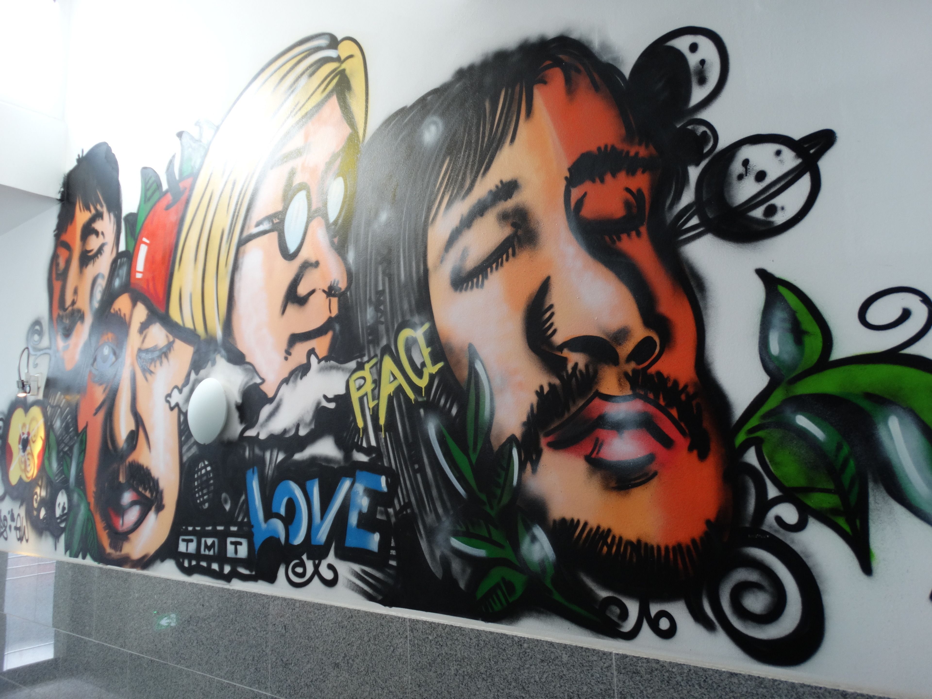Eine Wand mit einem großen Wandbild, das Gesichter und die Wörter „PEACE LOVE“ zeigt.