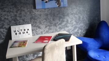 A room with a white desk, a blue chair, a painting of a woman on a scooter, and a sign that reads "ULTRA BOOK".