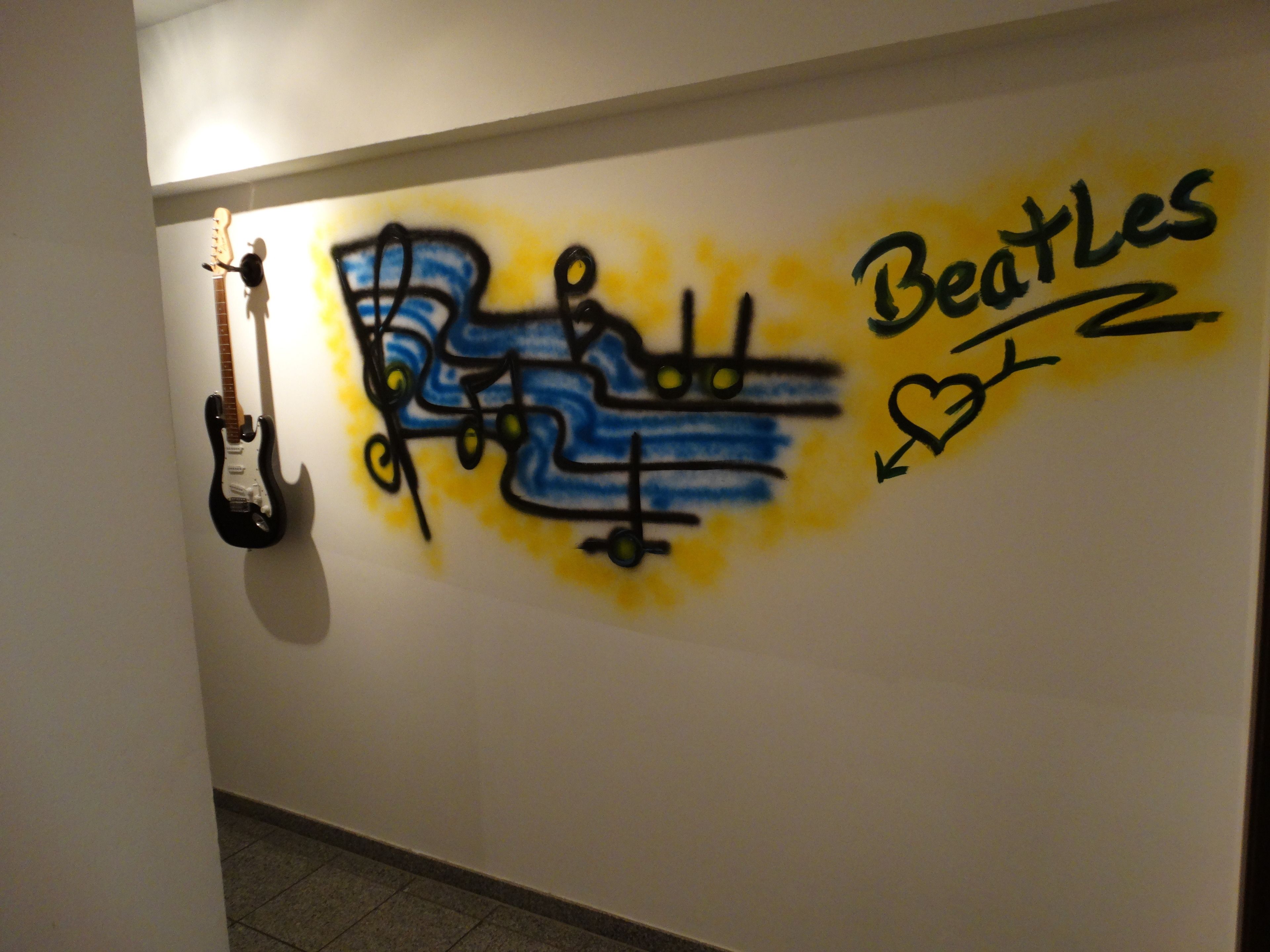 A wall with graffiti of a guitar and the words "Beatles" and "2" in a stylized font.