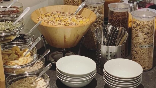 Un bufé con diferentes opciones de comida, como cereales, frutos secos y frutas. También hay cuencos y platos para servir.
