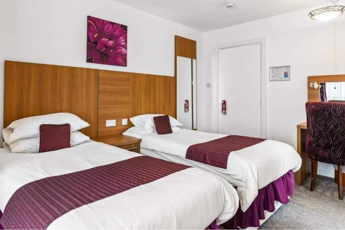 A hotel room with two beds, a wooden headboard, a mirror, a desk, and a chair.