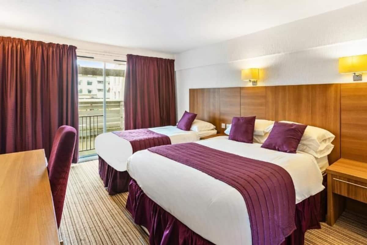 A hotel room with two beds, a wooden headboard, a small table, and a chair.