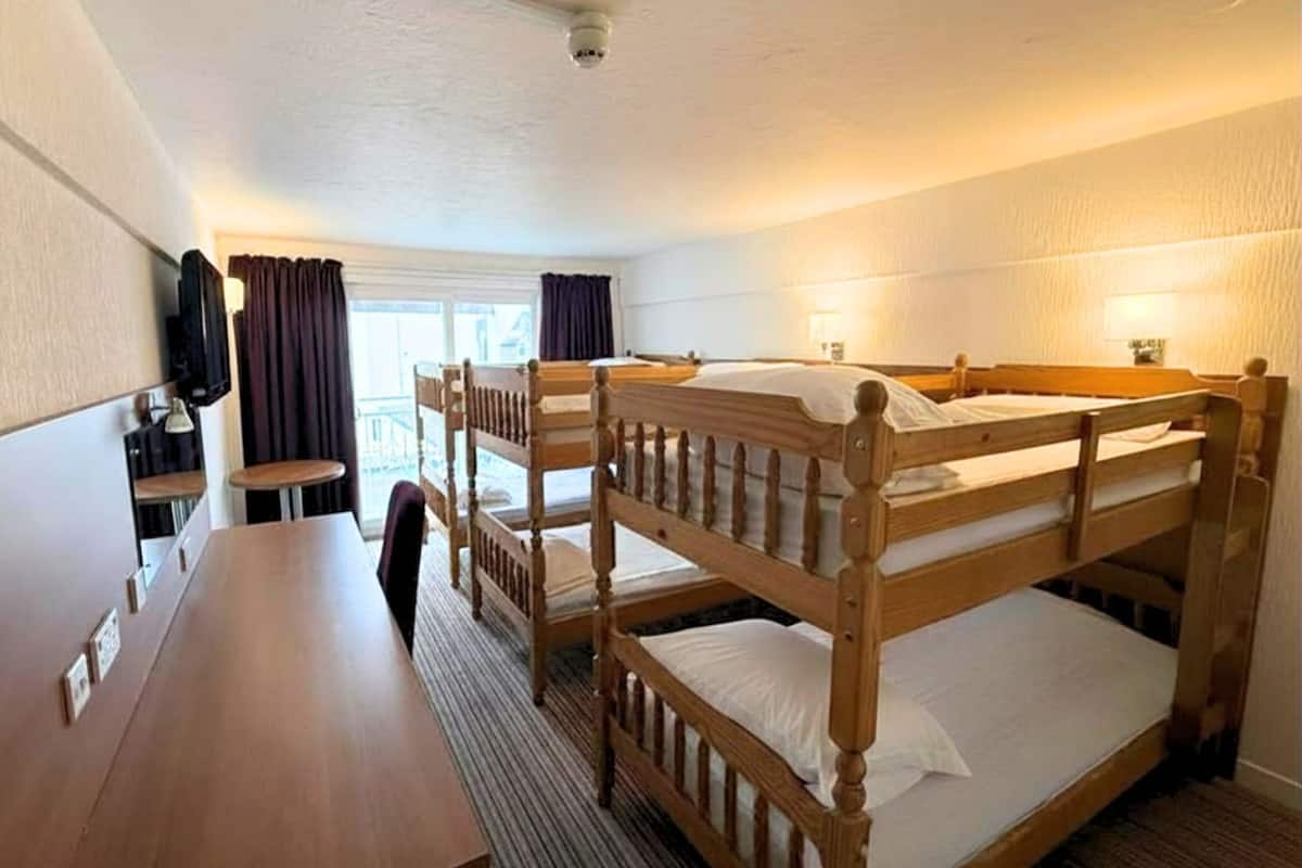 A bunk room with wooden bunk beds, a wooden table, and a TV mounted on the wall.