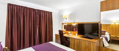 A hotel room with a bed, desk, TV, and a large window with curtains.