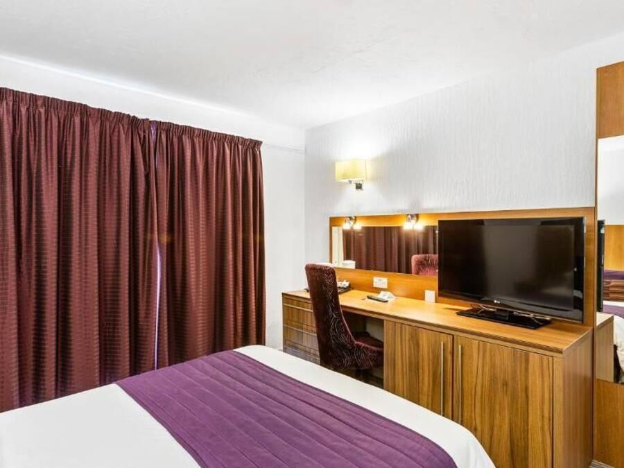 Een hotelkamer met een bed, bureau, televisie en een groot raam met gordijnen.