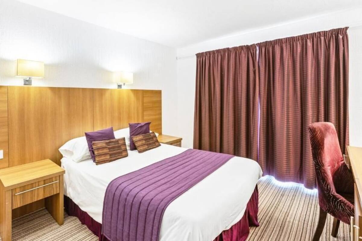 A hotel room with a bed, bedside tables, a chair, and a large window with curtains.