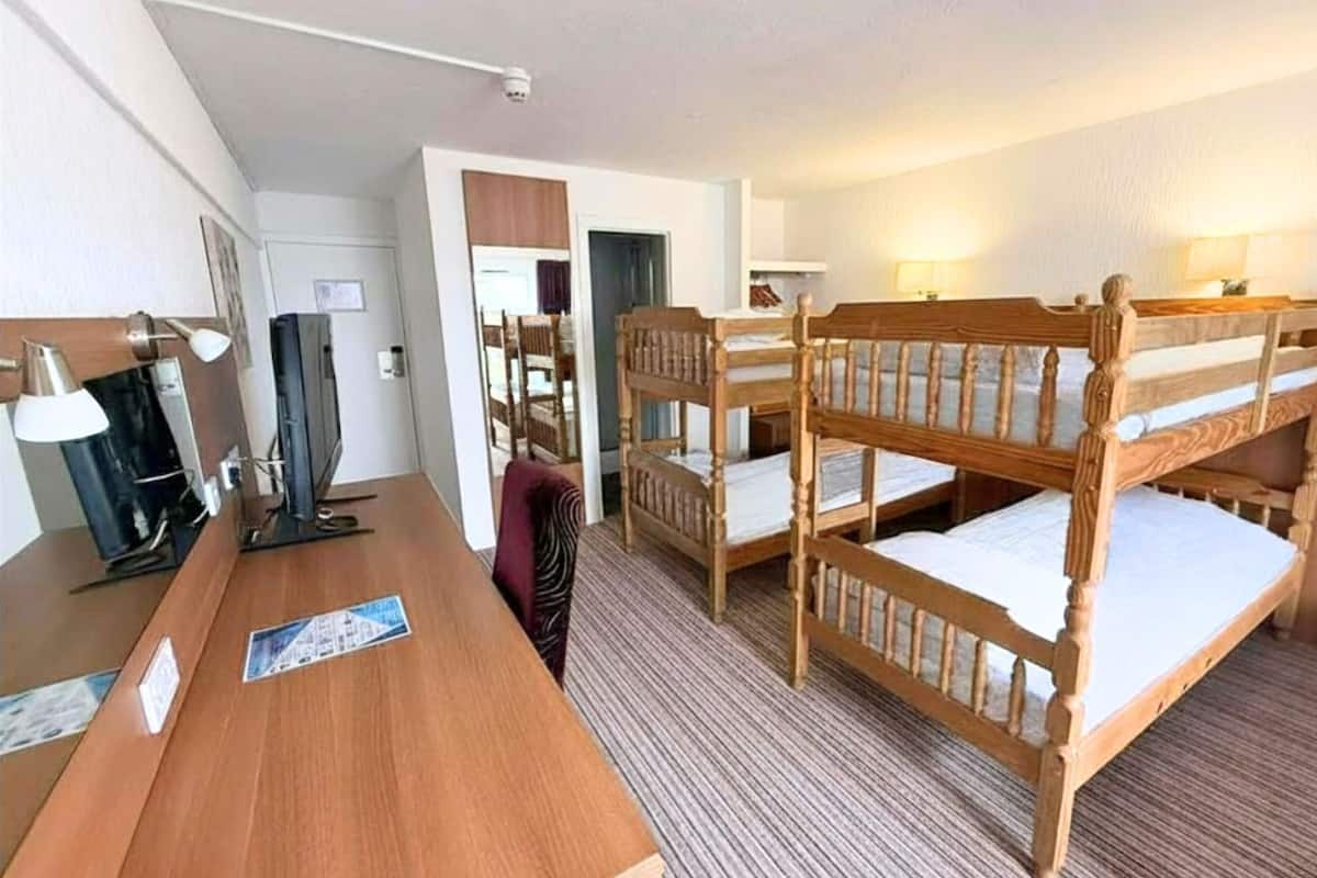 A hotel room with bunk beds, a wooden desk, a television, and a lamp.