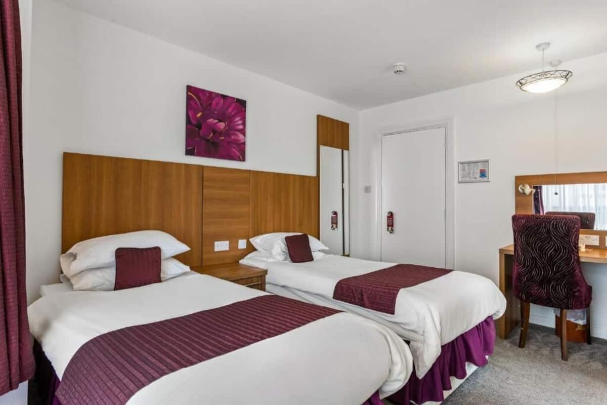 A hotel room with two beds, a wooden headboard, a desk with a chair, and a mirror.