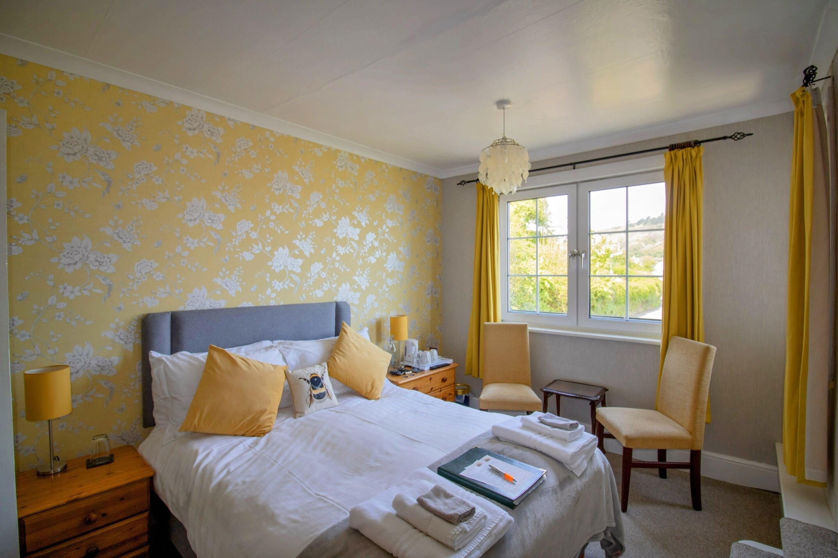 Une chambre d’hôtel avec un lit, des tables de chevet, une chaise, un bureau et une fenêtre avec des rideaux.