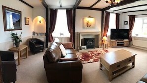 A living room with a fireplace, leather sofas, a coffee table, and a television. - Smugglers Rock House (Scarborough)