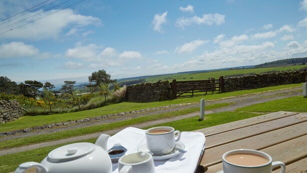 A picnic setup with a teapot, two cups, and a saucer on a wooden table, overlooking a rural landscape with a stone wall and a wooden fence. - Smugglers Rock House (Scarborough)