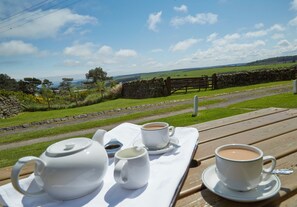 A picnic setup with a teapot, two cups, and a saucer on a wooden table, overlooking a rural landscape with a stone wall and a wooden fence. - Smugglers Rock House (Scarborough)