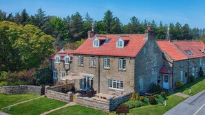 A stone building with a red-tiled roof, multiple windows, and a patio area with outdoor furniture. - Smugglers Rock House (Scarborough)