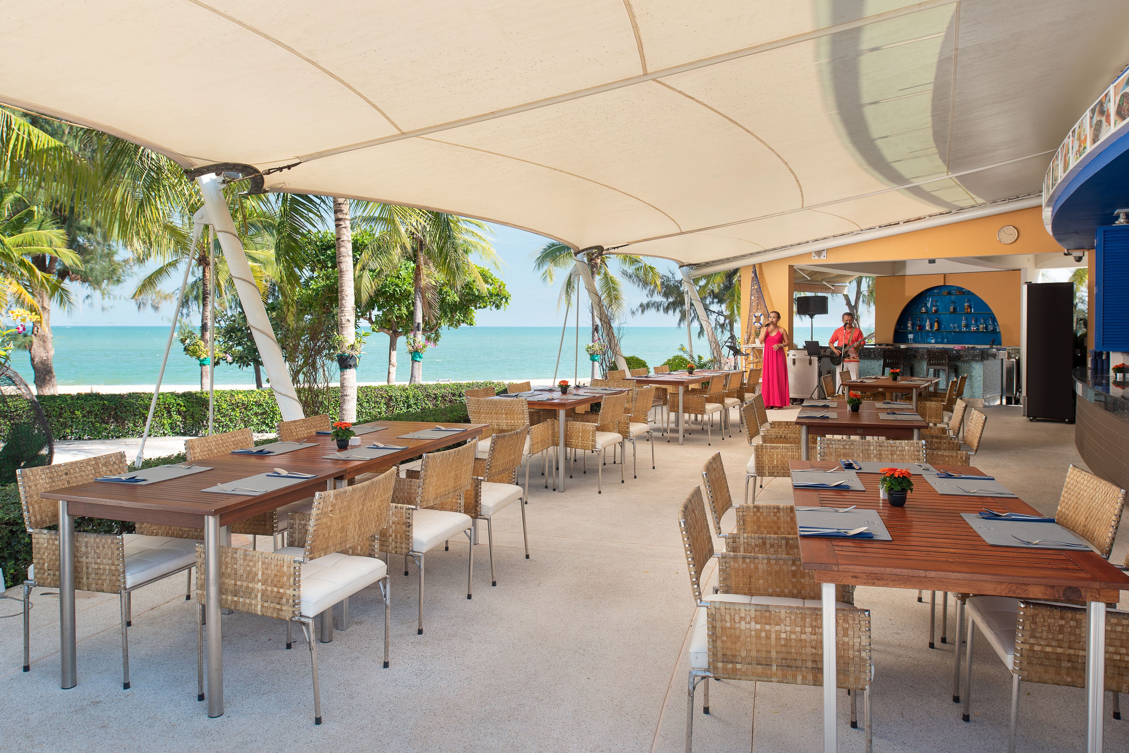 An outdoor restaurant with tables and chairs, a bar area, and a view of the ocean.