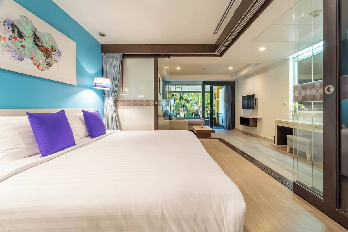 A modern hotel room with a large bed, a desk, and a glass partition.