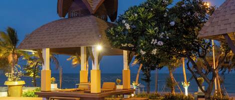 A beachside gazebo with seating and a view of the ocean.