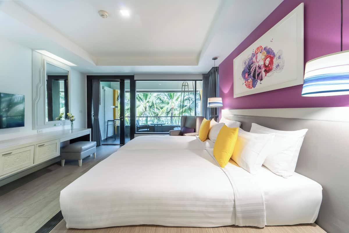 A modern hotel room with a large bed, a TV, a desk, and a view of palm trees.