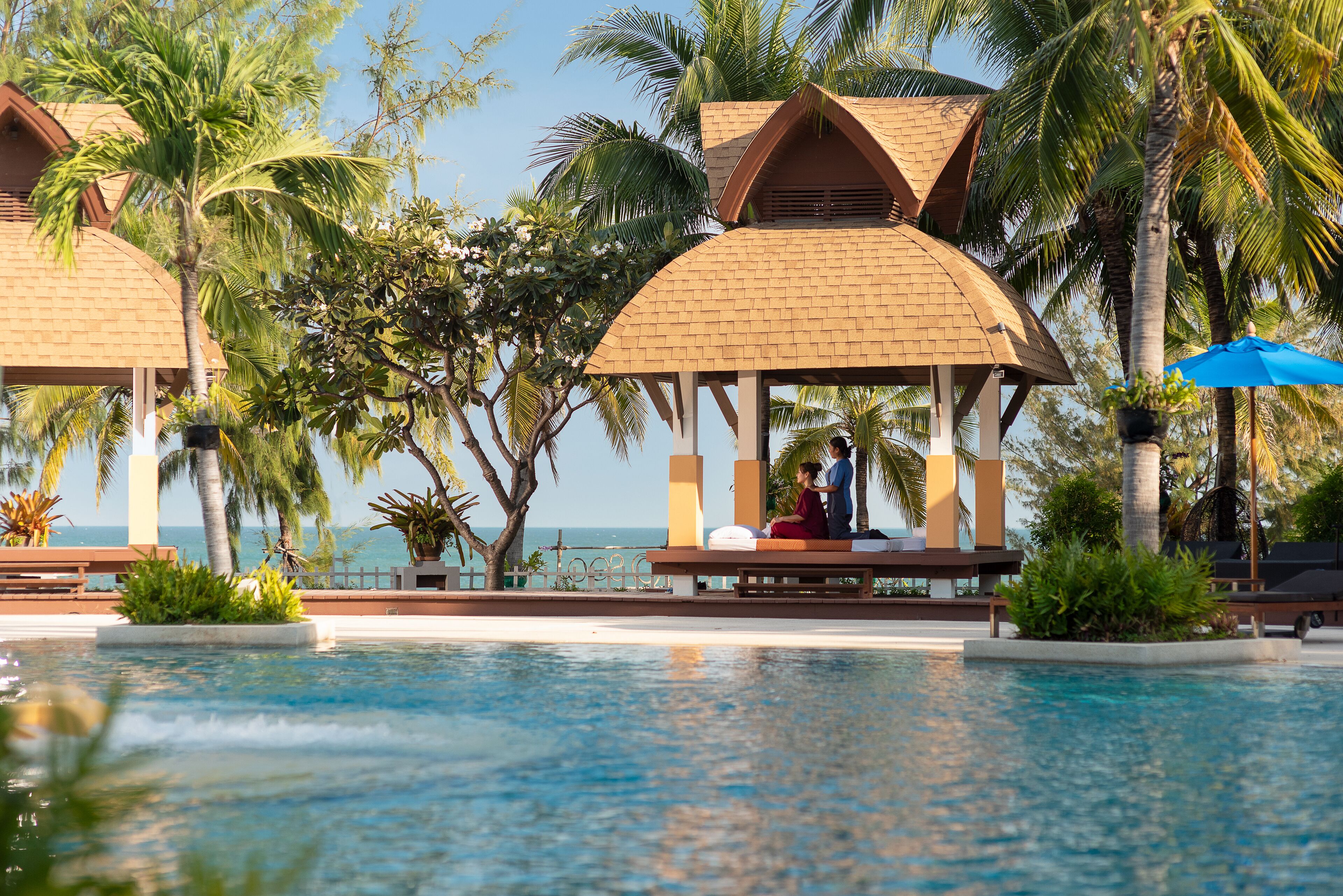 A pool area with a gazebo, palm trees, and a view of the ocean.