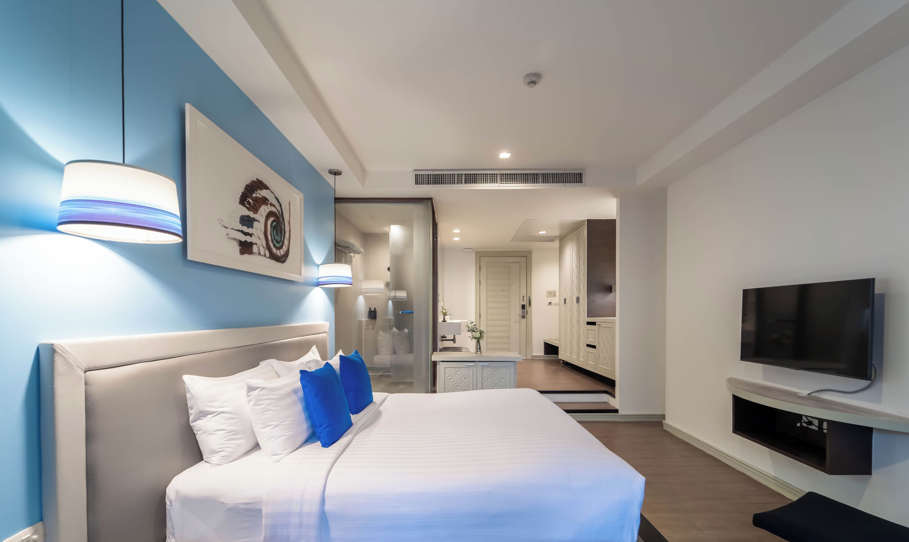 Quarto de hotel moderno com uma cama grande, uma TV fixada na parede e um banheiro visível por uma porta aberta.