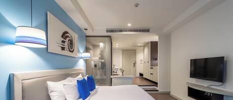 Una habitación de hotel moderna con una cama grande, un televisor montado en la pared y un baño visible a través de una puerta abierta.