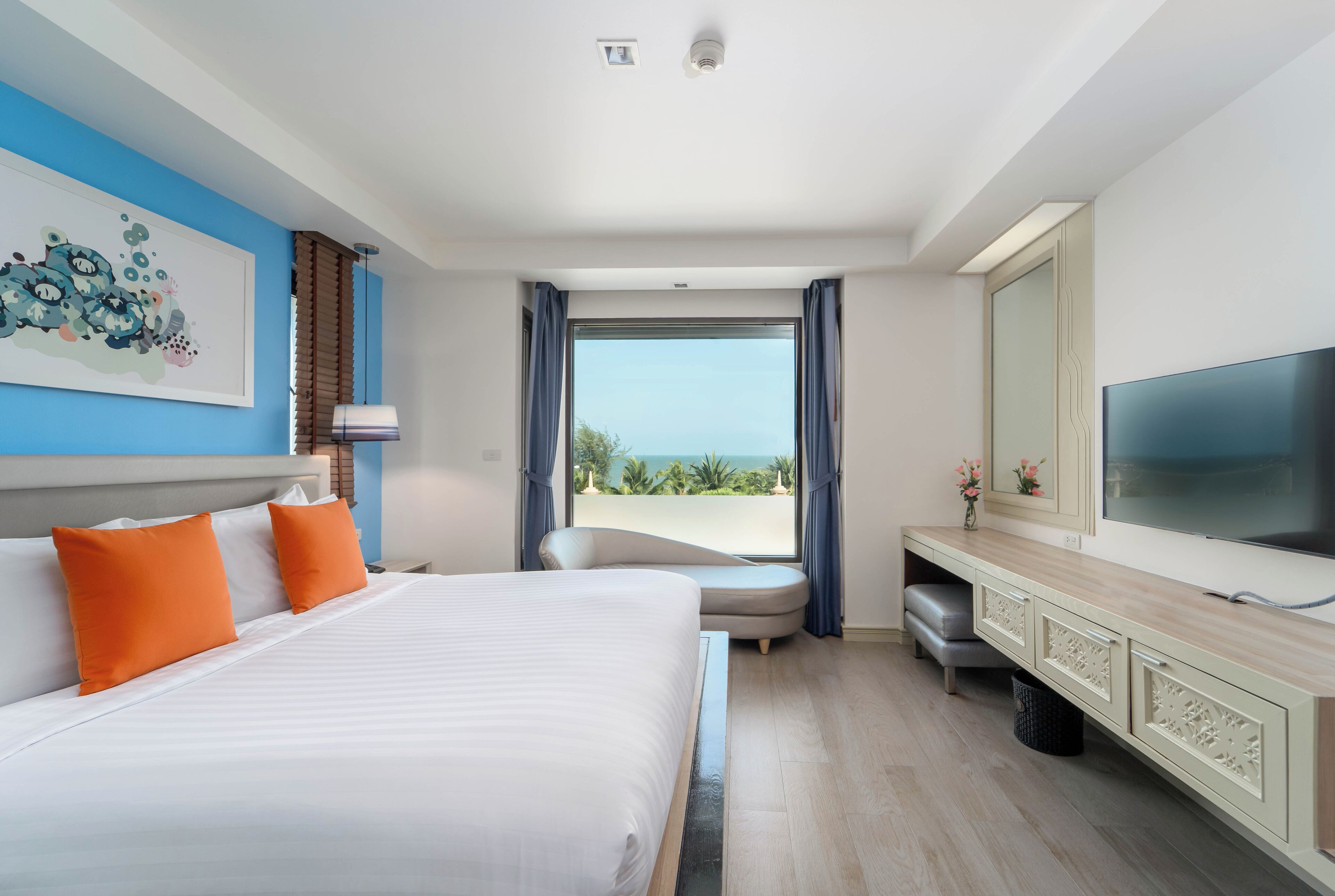 A hotel room with a large bed, a TV, a desk, and a view of the ocean.
