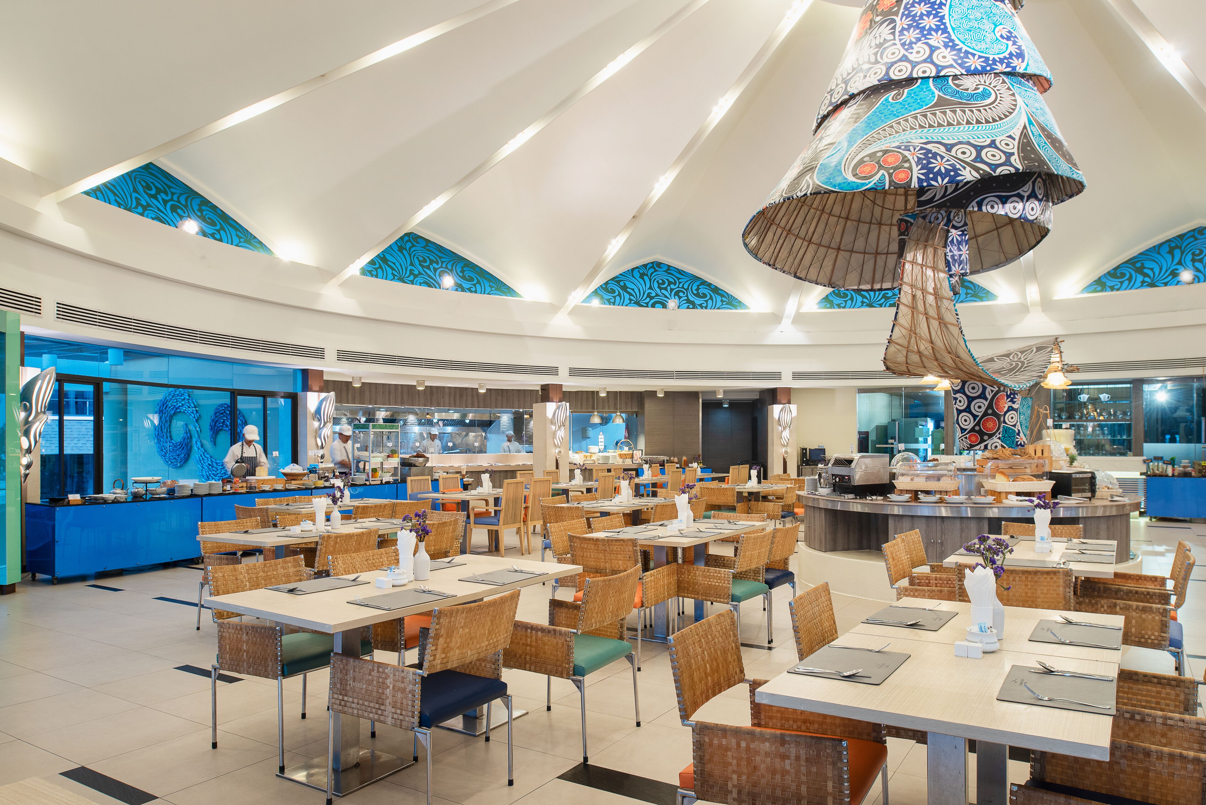 A spacious restaurant with high ceilings, blue patterned walls, and a central dining area with tables and chairs.