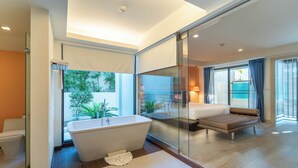 Une salle de bain moderne avec une baignoire sur pieds, une douche en verre et une grande fenêtre donnant sur la verdure à l’extérieur.