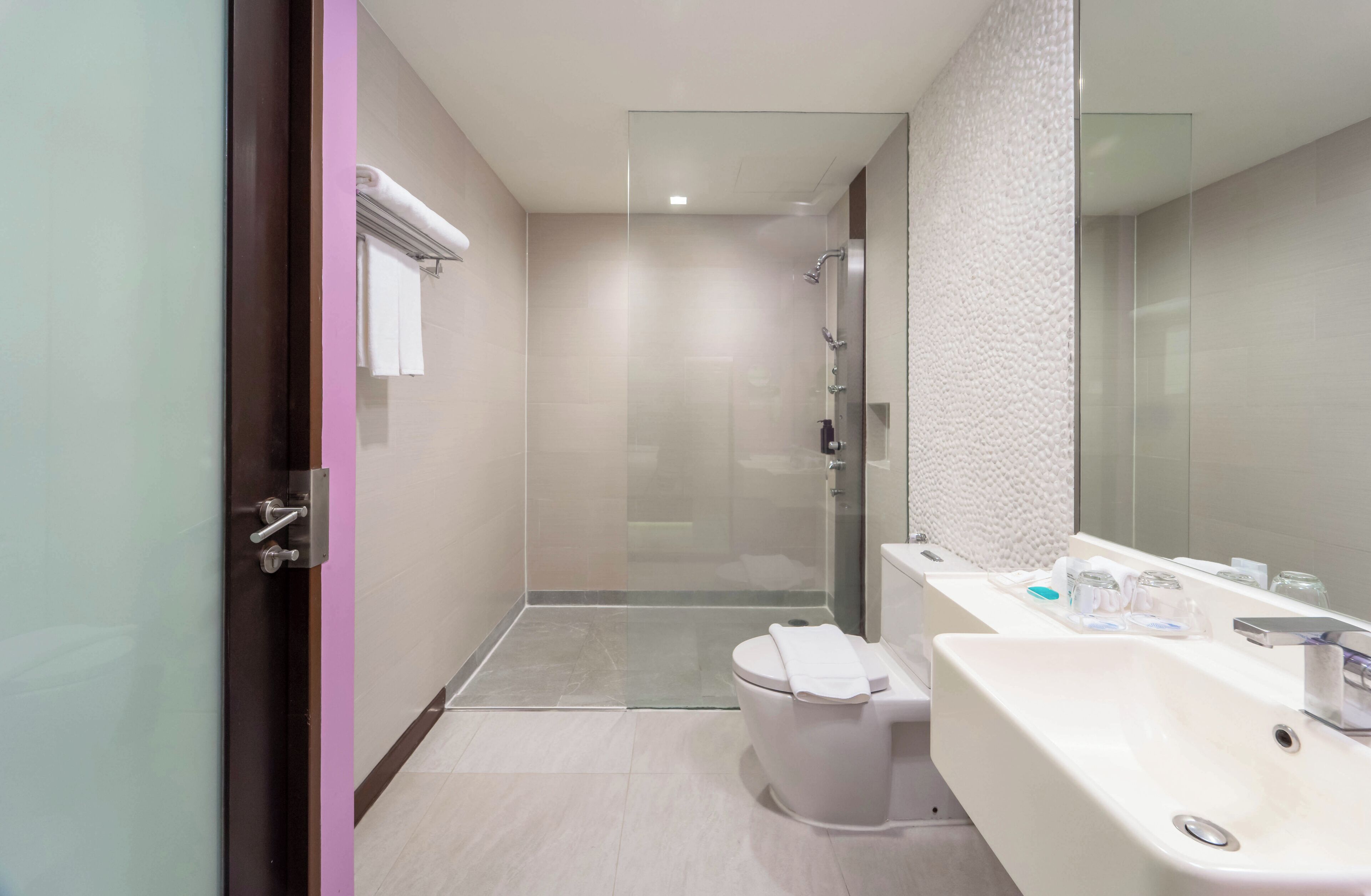 Une salle de bain moderne avec une douche à parois de verre, un lavabo blanc agrémenté d’articles de toilette et des toilettes sur lesquelles est posée une serviette.
