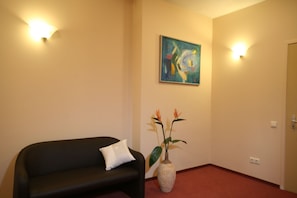 A room with a black sofa, a white pillow, a vase with flowers, and a painting on the wall. - Hotel Edvards (Riga)