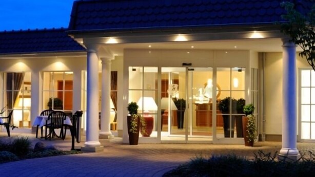 A hotel entrance with a covered patio, columns, and a well-lit interior visible through glass doors. - Waldhotel Nachtigall (Paderborn)