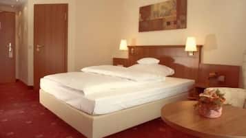 Una habitación de hotel con una cama, dos lámparas de noche, un cuadro en la pared y una mesita redonda con un florero.