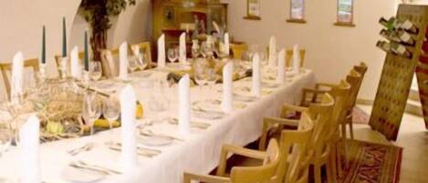 A long dining table set with white tablecloths, candles, and chairs.